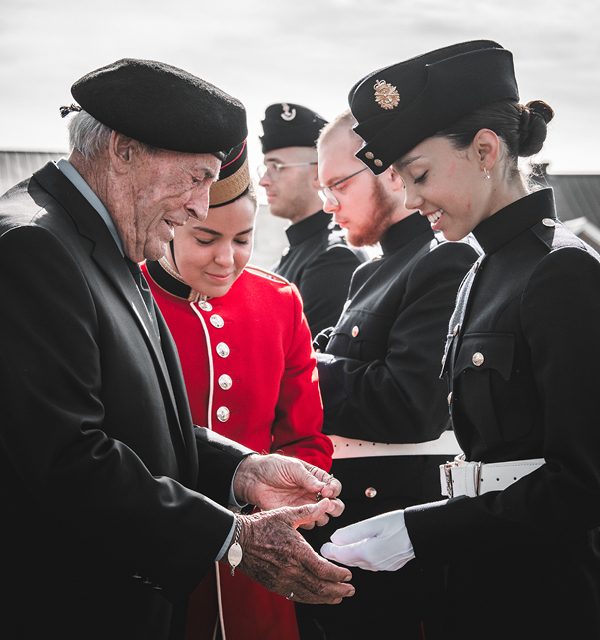 Un ancien commandant du CMR et ancien élève-officier remet des insignes du CMR aux élèves-officiers de première année sur le terrain de parade, sous le regard d'une élève-officière sénior.