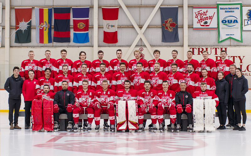 Three rows of men's hockey players with support staff on the side and coaches and captains in the front row. 