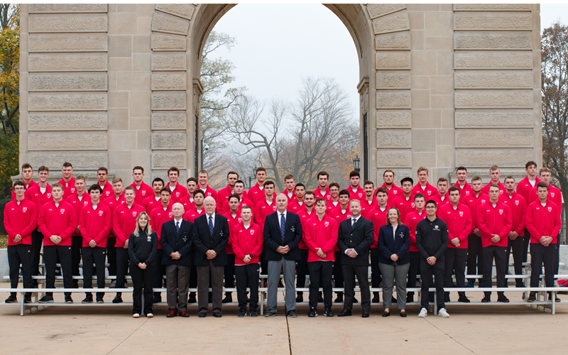 In front of the Memorial Arch, there are three rows of men's rugby players with coaches and support staff in the front.