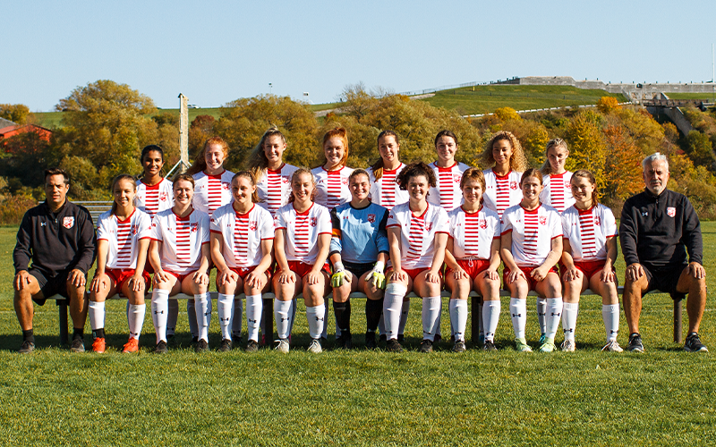 17 women's soccer players with two coaches with the front row being seated while the back row is standing. 