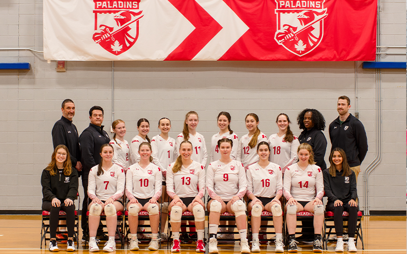 13 joueuses de volleyball, leur personnel d'encadrement et leurs entraîneurs devant la bannière des Paladins.